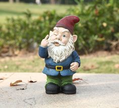 a gnome figurine sitting on the ground in front of some bushes and trees