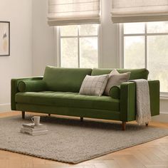 a green couch sitting on top of a rug in a living room next to two windows