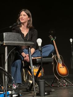 a woman sitting in front of a microphone on top of a stage next to guitars