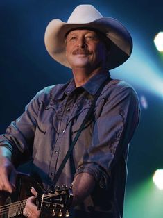 a man wearing a cowboy hat and holding a guitar in front of some spotlights