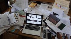 an open laptop computer sitting on top of a wooden desk covered in papers and books