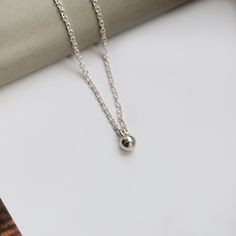 "Dainty Sterling Silver Ball Charm Necklace. Sterling silver necklace featuring a mini ball charm, on a fine sterling silver chain. A simple design that is perfect for both everyday wear and special occasions, a versatile piece to add to your jewellery collection. Wear alone or as a layering necklace. This necklace makes a wonderful gift and arrives in a cotton gift pouch.  - Details - *  Chain - 925 sterling silver *  Charm - 925 sterling silver *  Chain stamped 925 *  Charm size  4mm *  Chain lengths available - 16\" and 18\" *  In a reusable cotton gift pouch Please choose your preferred chain length from the drop down bar. . . . . . . . . . . . . . . . . . . . . . . . . . . . . . . . . . . .  - You may also like -  More sterling silver necklaces - https://www.etsy.com/uk/shop/EmmaLouJe Minimalist Silver Necklace With Dangling Charms, Silver Round Minimalist Charms, Round Sterling Silver Minimalist Charm Necklace, Minimalist Silver Necklace With Moon Charm, Tiny Minimalist Sterling Silver Charm Necklaces, Silver Ball Necklace, Cleaning Silver Jewelry, Ball Necklace, Cotton Gifts