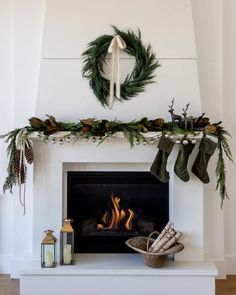 a white fireplace with stockings and wreaths on it's mantel above the fire