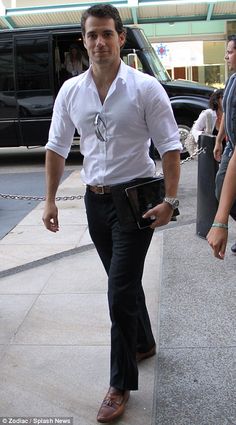 a man in white shirt and black pants walking down the street with his hand on his hip