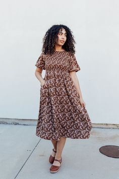 Stay stylish with the Emsley Midi dress! Featuring a charming brown color with delicate white florals, this dress is designed with a smocked bodice and flared bubble sleeves for a fun and flattering look. Plus, it has pockets for added convenience. Look effortlessly chic in this must-have dress! The Emsley Midi is lined. Fits true to size. Model is wearing a small and is 5'10". Plus model is wearing a 2X and is 5'6". Size Chart Length Bust Waist S 46" 30" 28" M 46" 32" 30" L 47" 34" 32" XL 48" 3 Casual Floral Dress With Gathered Sleeves, Spring Brown Dress With Gathered Sleeves, Brown Spring Dress With Pockets, Brown Smocked Bodice Dress For Day Out, Brown Spring Midi Dress With Pockets, Brown Spring Dress With Gathered Sleeves, Spring Fitted Brown Smocked Dress, Brown Midi Length Dress With Smocked Back, Brown Dress With Smocked Bodice And Short Sleeves