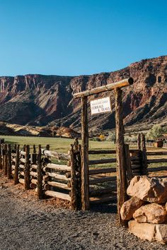 a wooden gate with a sign on it in front of mountains and dirt road leading into the distance