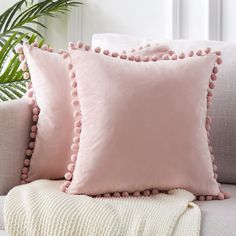 two pink pillows sitting on top of a couch next to a potted palm tree