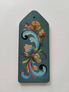 a green tag with colorful flowers painted on it's front and back sides, hanging from the wall