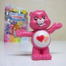 a pink toy bear holding a heart shaped object in front of a candy bar bag