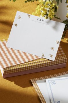 two folded cards sitting on top of each other next to some yellow flowers and papers