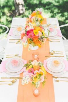 a long table with plates and flowers on it is set for an outdoor dinner party