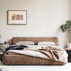 a bed with blankets on it next to a table and potted plant in the corner