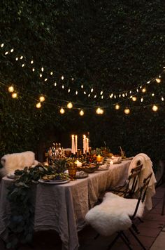 an outdoor dinner table with lights strung over it