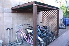 several bicycles are parked in a row under a pergolated shelter on the sidewalk