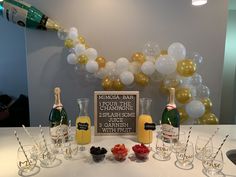 a table topped with champagne bottles and glasses filled with fruit next to a balloon arch