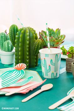 a table topped with plates and cups filled with succulents next to cactus plants