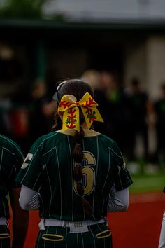 two girls in uniforms with bows on their heads are walking together at a baseball game