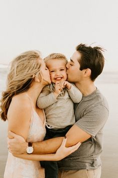 a man and woman kissing their son on the beach