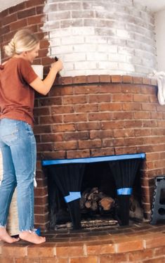 a woman painting a brick fireplace with blue tape