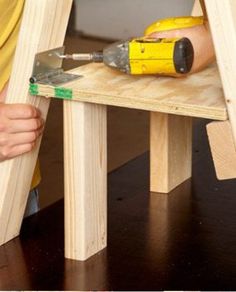 a person using a drill to attach the legs of a wooden step stool with tools on it