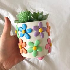 a hand holding a flower pot with flowers painted on it