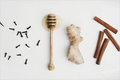 an assortment of spices including ginger, cinnamon sticks and honey on a white plate with a wooden spoon