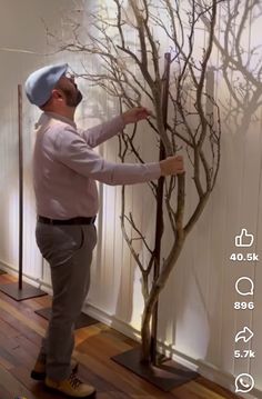 a man is standing in front of a fake tree with no leaves on it and reaching for the branches