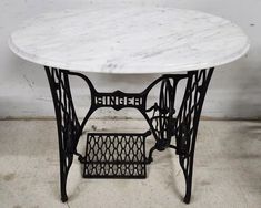 a white marble table with black iron legs and an intricate design on the top, sitting in a room