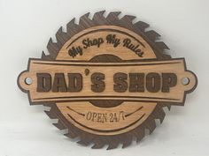 a wooden sign that says dad's shop with a circular saw blade on it