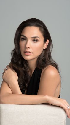 a beautiful young woman sitting on top of a white chair with her arms crossed and looking at the camera