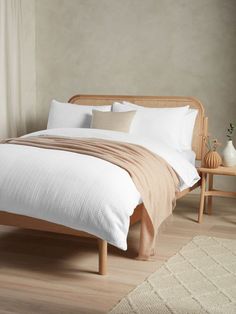 a bed with white sheets and pillows on top of it next to a wooden table