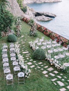 an outdoor wedding set up with chairs and flowers on the lawn next to the water