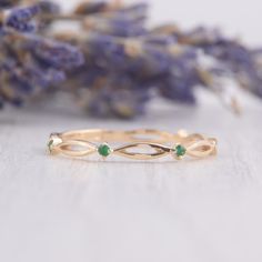 a gold ring with two green stones on it and some lavender flowers in the background