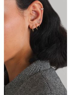 a woman with black hair wearing ear piercings and a grey jacket, looking off to the side