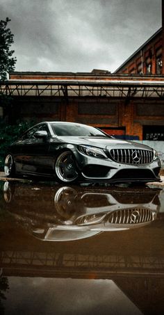 a black car is parked in front of a building with its reflection on the ground