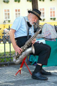 an old man sitting on a stool playing a saxophone in front of a fenced area