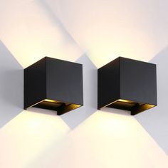 two square lights are on the wall in front of a white wall and one is black