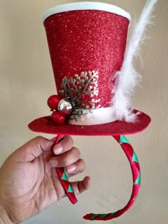 a hand holding a red top hat with white feathers and decorations on it's side