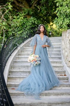 a woman in a blue dress is standing on some stairs with flowers and greenery