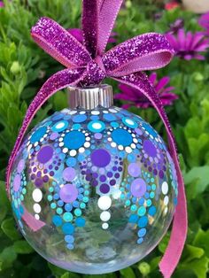 a glass ornament with purple ribbon and polka dot design on the top, sitting in front of some flowers