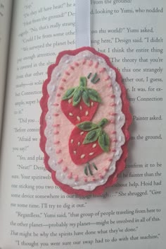 the book is open to show an embroidered brooch with two strawberries on it