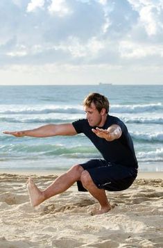 a man is stretching on the beach with his arms out to catch a frisbee