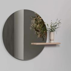 a round mirror sitting on top of a wall next to a vase filled with flowers