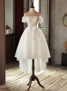 a white dress on a mannequin stand in a room with wooden flooring