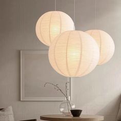 three white lanterns hanging from the ceiling above a table with chairs and a vase on it