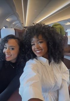 two women sitting on an airplane with their arms around each other and smiling at the camera