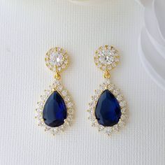 Gold Clip-On Earrings with Blue Drops for Brides & Bridesmaids A beautiful pair of gold earrings with clip on's combined with blue teardrops, The earrings look rich and elegant on brides, bridesmaids, and on every woman with her favorite outfit. The gold clip earrings are comfortable, with a sapphire blue teardrop and round ear top. The earrings are made of high-quality cubic zirconia, making them super sparkly and highly reflective. The earrings are available in three finishes of rose gold, yel Sapphire Blue Earrings, Blue Earrings Wedding, Blue And Gold Wedding, Gold Wedding Earrings, Blue Bridal Earrings, Dark Blue Earrings, Blue Jewelry Set, Earrings Sapphire, Blue Pendant Necklace