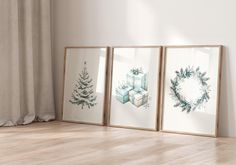 three framed art pieces on the floor in front of a window with a christmas wreath