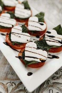 several slices of tomato and mozzarella on a white plate with leafy greens