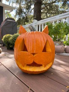 a carved pumpkin with a cat's face on the outside of it, sitting on a wooden deck